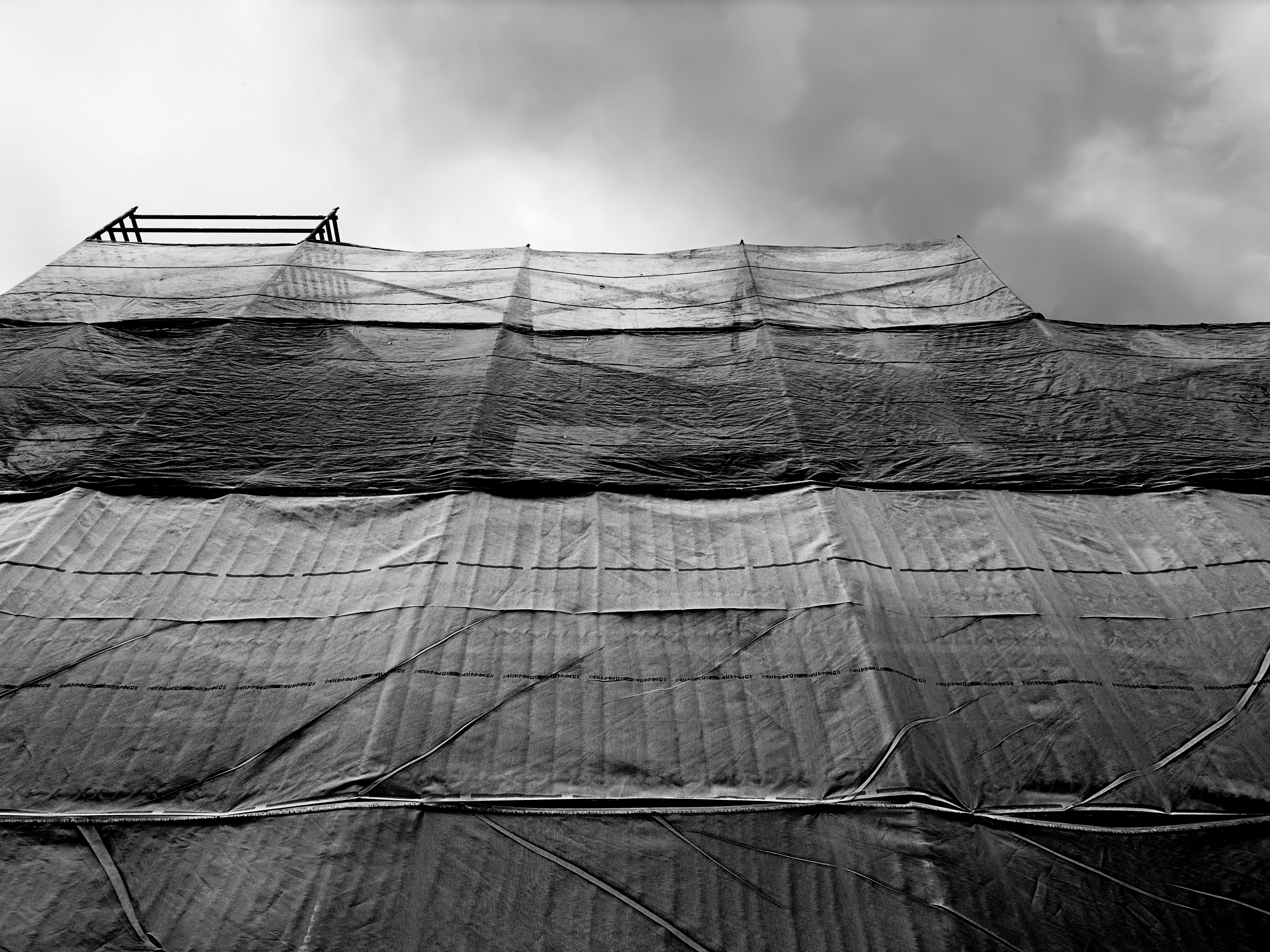 Monochrome view of a building covered in protective sheeting against a cloudy sky
