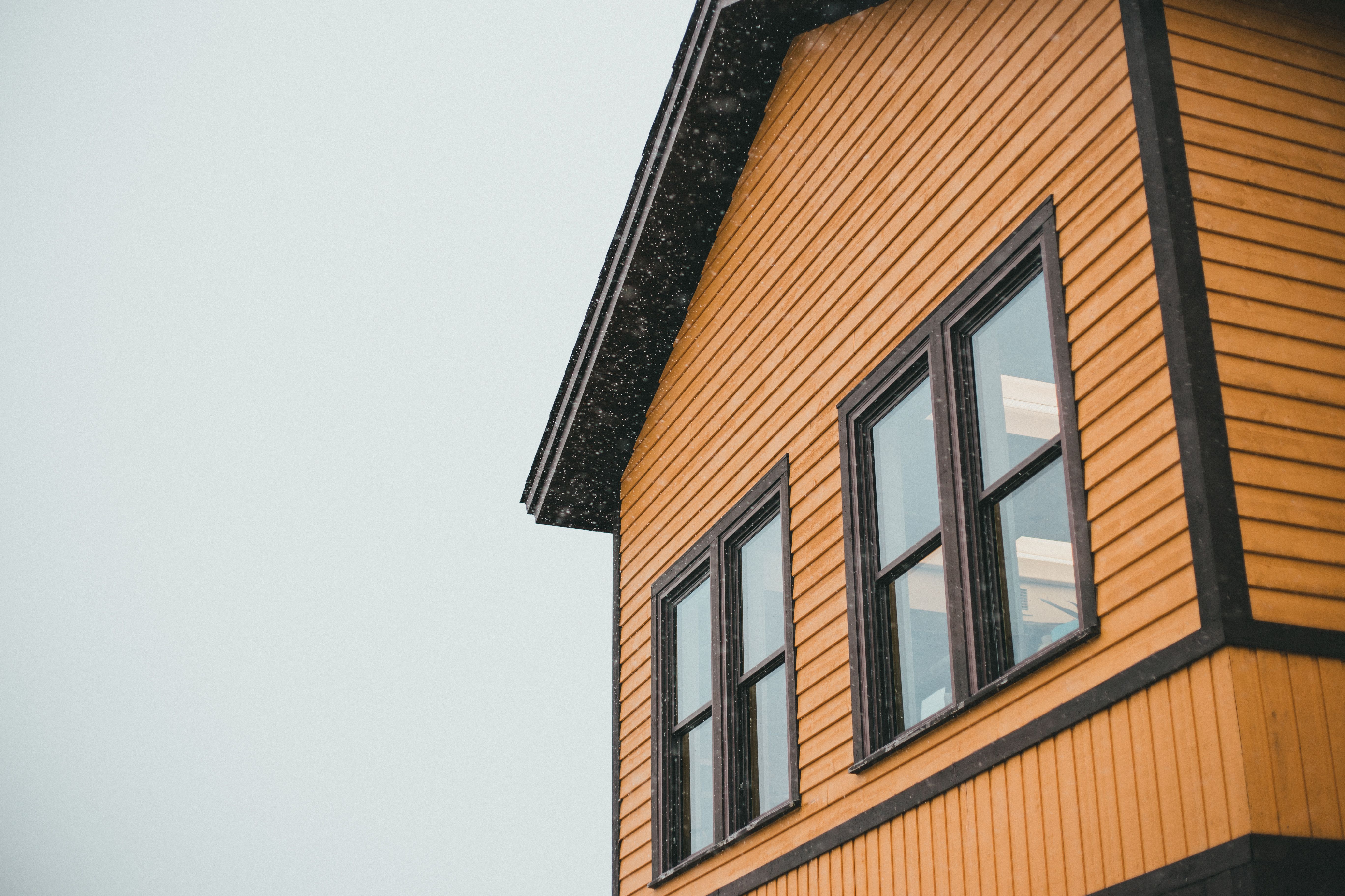 Close-up of a yellow wooden house with black trim and falling snow
